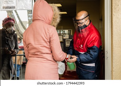 Cape Town, South Africa - August 2020: Post Office Worker Wearing Protective Mask And Face Shield Spraying Hand Sanitizer N Client Collecting Covid 19 Relief Funds