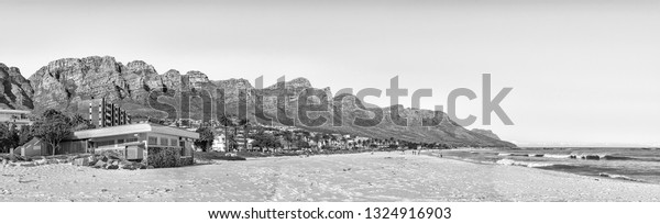 CAPE TOWN,\
SOUTH AFRICA, AUGUST 9, 2018: Panorama of a beach in Camps Bay in\
Cape Town in the Western Cape Province. The 12 Apostles, people and\
buildings are visible.\
Monochrome