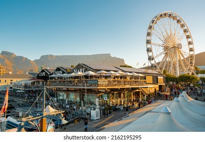 CAPE TOWN, SOUTH AFRICA - February 11, 2022: View of Cape Wheel and restaurants in Cape Union Mart with Table Mountain in the background at sunset.