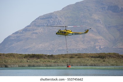 CAPE TOWN, SOUTH AFRICA - JAN 11 2017. Helicopter Being Used To Collect Water From A Local Lake To Fight Wild Fire In The Mountains Behind The Glencairn Suburb Of Cape Town.