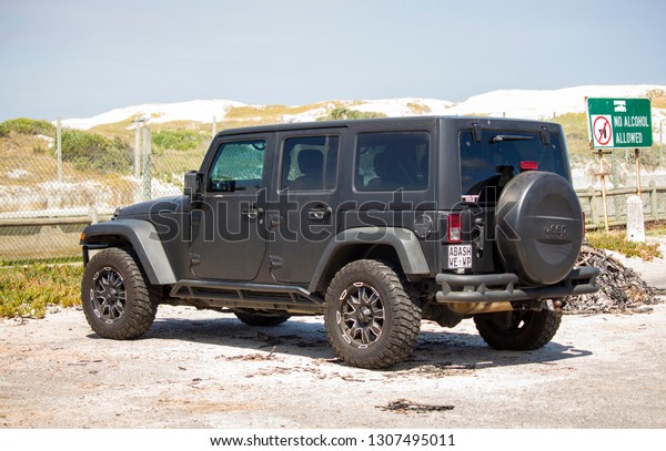 Cape Town, South Africa - January 8, 2019:\
Close-up black car JEEP Wrangler on the parking next to the\
Muizenberg beach. Side view of the 4x4 legendary vehicle. Offroader\
for the extreme activity.