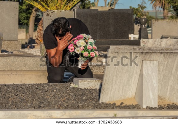 Cape Town, South Africa - January 2021: Mixed\
race man, sad and depressed at the funeral of a loved one due to\
Covid 19, Corona Virus Mental Health during Covid 19 Pandemic.\
Covid 19 funeral.
