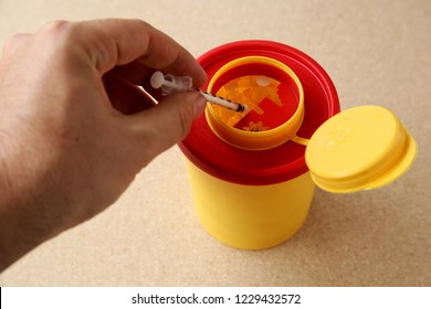 Cape Town, South Africa - November 13, 2018: A Red And Yellow Medical Waste Container Filled With Used Syringes On A Wooden Table. 