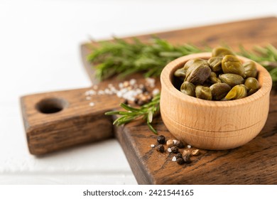 Capers in a bowl on a wooden kitchen table. Capers with sea salt and rosemary. Pickled capers.Mediterranean cuisine ingredient. Organic spices and seasonings. Copy space. - Powered by Shutterstock