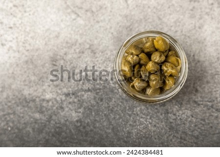 Capers in a glass jar on a wooden kitchen table. Capers with sea salt and rosemary. Pickled capers.Mediterranean cuisine ingredient. Organic spices and seasonings. Copy space.