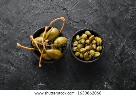 Capers. Marinated capers in a bowl on a black stone background. Top view. Free space for your text.