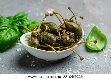 Capers. Marinated or pickled canned capers fruit with fresh basil leaves in a small bowl, on gray background. Long banner format. top view.