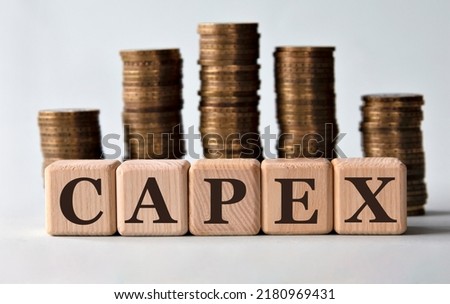 CAPEX - acronym on wooden cubes on the background of stacks of coins. Capital cost concept