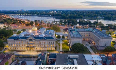 The capital statehouse of New Jersey lights up as the sun sets the Delaware River in the background city of Trenton