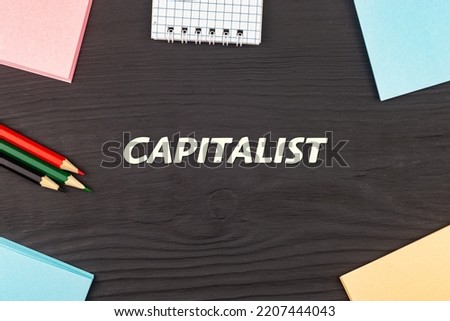 CAPITALIST - text, stickers and colored pencils on a black wooden table. Business concept: buying, selling, commerce (copy space).