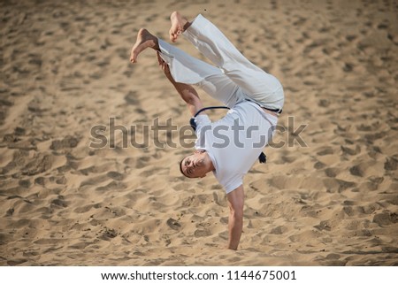 capoeira dancer posing, performing a handstand, on the background of desert and sand