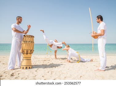 Capoeira Team Training On The Beach - Martial Arts Athletes Performing Stunts While Two Men Play Music