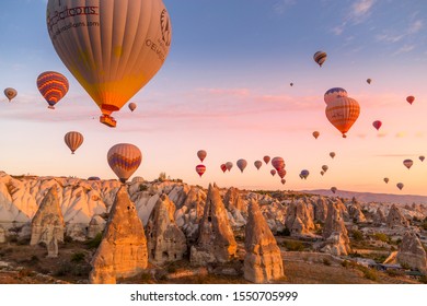 Göreme, Cappadocia, Turkey - October 7 2019:  Hot air balloons filled with tourists during a pink sunrise floating along valleys of Göreme National Park