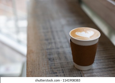 Cappuccino With Beautiful Heart Shape Latte Art In The Paper To-go Cup. Take Away Coffee Concept. Wooden Rustic Background, Loft Space. Copy Space For Your Text. Side-view