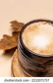 Cappuccino Coffee In A Ceramic Cup, Top View. Milk Foam, Texture. Cappuccino On An Autumn Background With Foliage On A Beige Background.