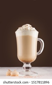 Cappuccino coffee in elegant glass with whipped cream, cocoa powder and cookies on white table and dark brown wall, vertical.