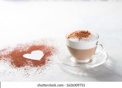 Cappuccino and heart made of cocoa powder on white background. The idea for a festive breakfast, Valentine's Day. Selective focus, copy spacy