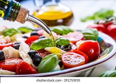 Caprese Italian or Mediterranean salad. Tomato mozzarella basil leaves black olives and olive oil on wooden table.