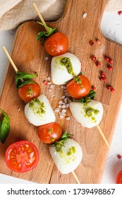 Caprese Salad On Sticks Cherry Tomatoes, Mozzarella Cheese, Basil, Pesto Sauce On Wood Board Over White Rustic Background Top View Close Up