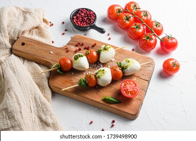 Caprese Salad On Sticks Cherry Tomatoes, Mozzarella Cheese, Basil, Pesto Sauce On Wood Board Over White Rustic Background