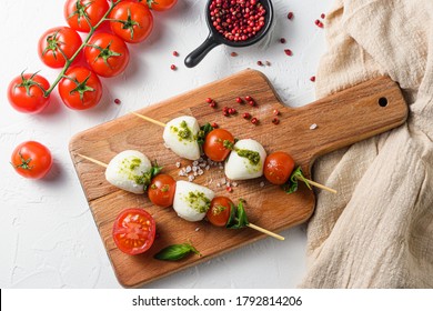 Caprese Salad On Sticks Cherry Tomatoes, Mozzarella Cheese, Basil, Pesto Sauce On Wood Board Over White Rustic Background Top View