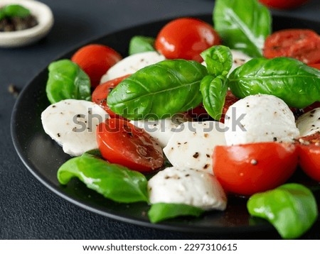 Caprese salad with ripe tomatoes and mozzarella cheese with fresh basil leaves on black background. Italian food. Close-up