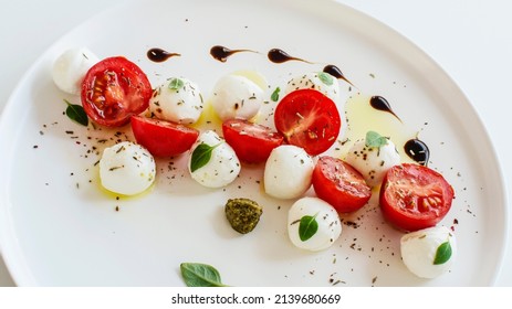 Caprese salad traditional Italian food on a white plate close-up. Mozzarella and cherry tomatoes with herbs and balsamic, pesto sauce