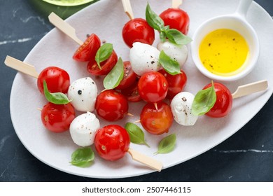 Caprese skewers with mozzarella balls, cherry tomatoes and green basil on a white plate, middle close-up, horizontal shot - Powered by Shutterstock