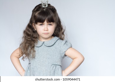 Capricious Child. Spoiled Little Girl With Crown On Head, Her Hands On Her Hips 