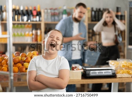Capricious little boy crying while his parents standing behind in despair in grocery store