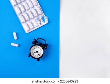 Capsule Pills In Blister Pack And Alarm Clock On Blue And White. Sleeping Pill With Melatonin And Taking Medicine By Schedule Concept. Medical And Pharmaceutical Flat Lay. Mockup Copy Space