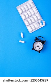 Capsule Pills In Blister Pack And Alarm Clock On Blue Background. Sleeping Pill With Melatonin And Taking Medicine By Schedule Concept. Medical And Pharmaceutical Flat Lay