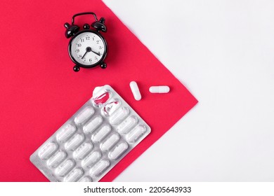 Capsule Pills In Blister Pack And Alarm Clock On Red And White. Sleeping Pill With Melatonin And Taking Medicine By Schedule Concept. Medical And Pharmaceutical Flat Lay. Mockup Copy Space