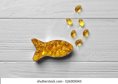 Capsules of cod liver oil arranged in a fish shape on white wooden background - Shutterstock ID 526305043