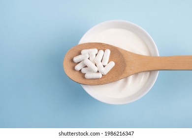 Capsules Probiotic On A Wooden Spoon And Bowl With Homemade Yogurt On Light Blue Background. Fermented Foods, Dairy, Nutritional Supplement, Healthy Digestion Concept. Top View, Flat Lay