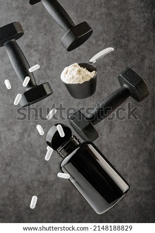 Capsules of sports supplements, a scoop with protein and dumbbells levitate on a dark background. The concept of sports nutrition and supplements. 商業照片 © 