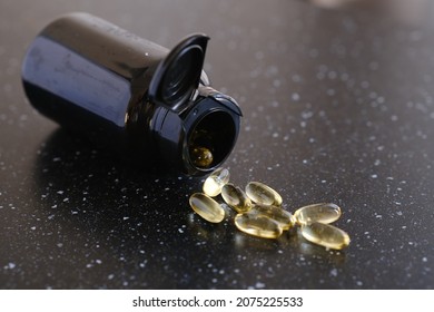 Capsules with vitamin E, omega 3, lying next to an open container on a black background. 