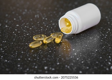 Capsules with vitamin E, omega 3, lying next to an open container on a black background. 