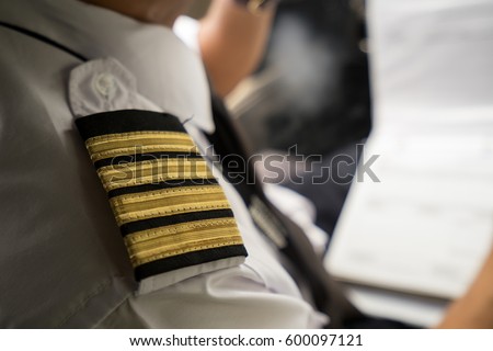 Captain in the aircraft cockpit writing a report after flight. Focusing on his pilot epaulets.