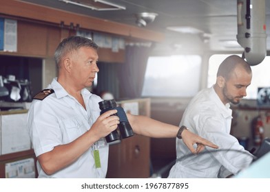 The Captain Of A Cargo Ship In A White Shirt And Shoulder Straps On The Bridge Gives Instructions To The Navigator