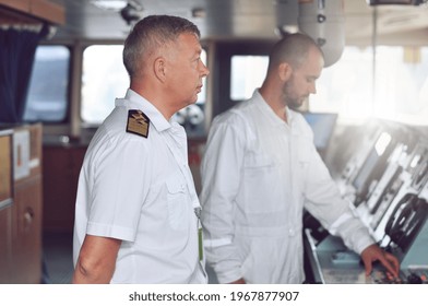 The captain of a cargo ship in a white shirt and shoulder straps on the bridge gives instructions to the navigator