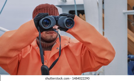 Captain Of Commercial Fishing Ship Dressed In Protective Coat Looking Through Binoculars