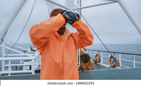 Captain Of Commercial Fishing Ship Dressed In Protective Coat Looking Through Binoculars