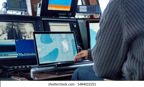 Captain Of Commercial Fishing Ship Surrounded By Monitors And Screens Working With Sea Maps In His Cabin.