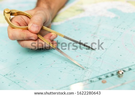 The captain measures the distance on the map with a compass. Close-up.