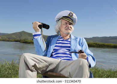 The captain on vacation looking through binoculars while sitting on the river bank