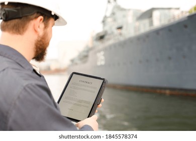 Captain reading contract on electronic book or tablet near vessel in background. Concept of maritime profession and modern technology.