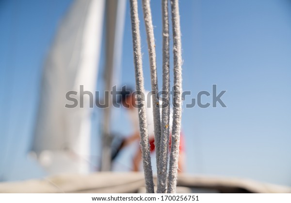 A captain rigging the sail on his\
sailboat. A rope is partly covering the frame and the sun is\
shining strong as he attaches the sail to the main mast.\
