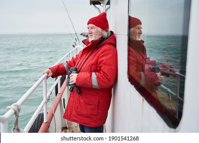 The Captain Of A Small Fishing Boat Holding His Binoculars While Looking Away. The Bearded Man Looking Very Determined. Wild Waves And Spray In The Background. Stock Photo