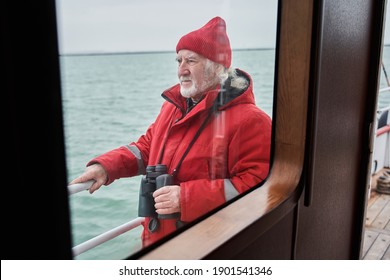 The Captain Of A Small Fishing Boat Holding His Binoculars While Looking Away. The Bearded Man Looking Very Determined. Wild Waves And Spray In The Background. Stock Photo